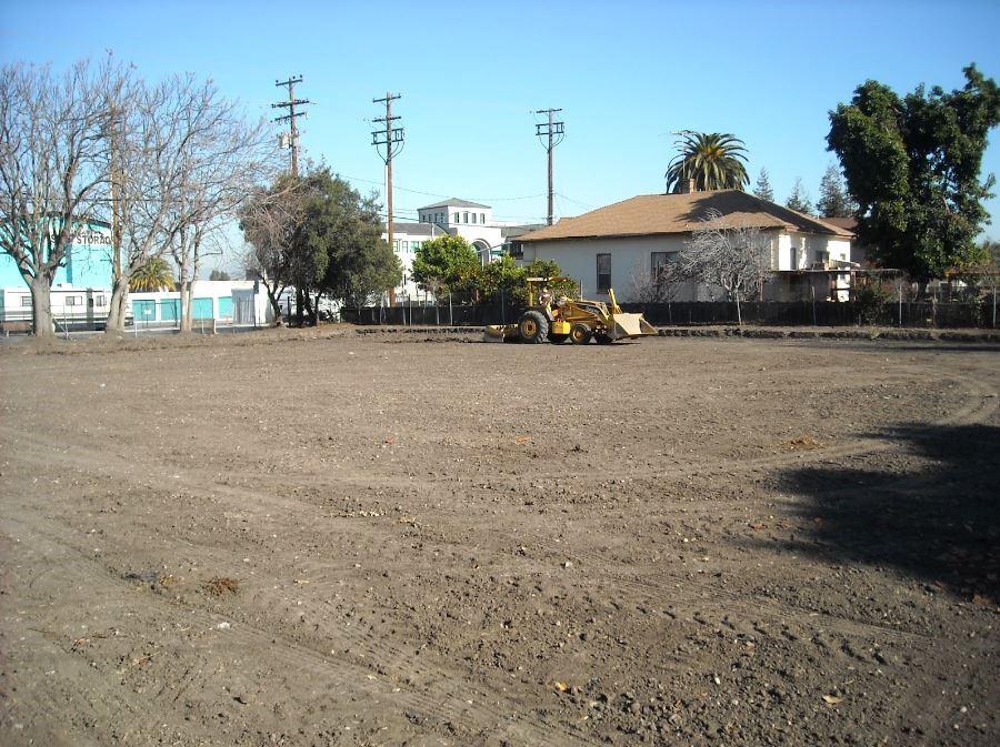 A field of flat dry dirt with a yellow front loader tractor in the background.
